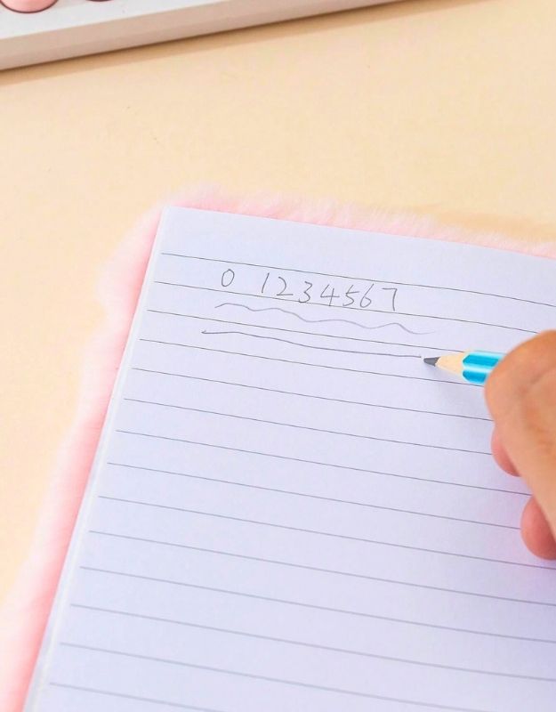 Hand writing numbers on a lined notebook with a pen.